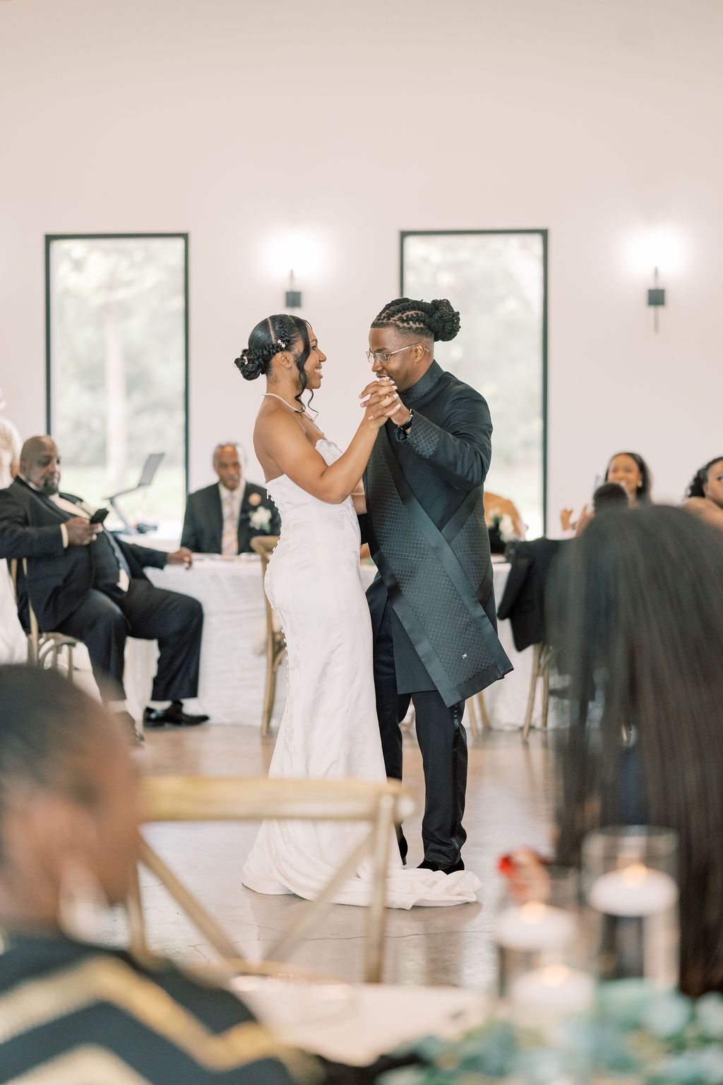 Bride and groom share their first dance at elegant wedding reception with guests seated around the dance floor.