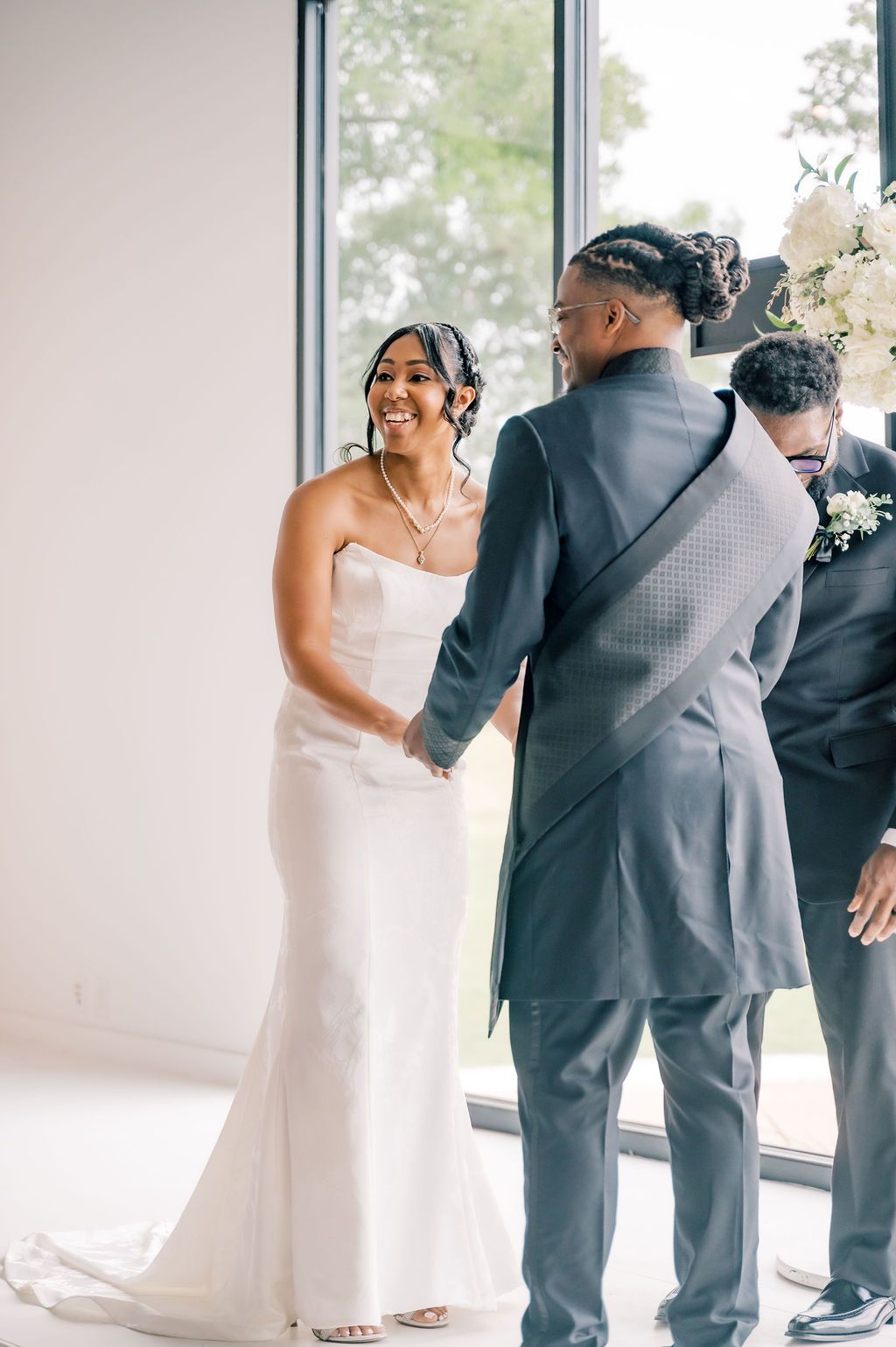 Bride in white gown smiles joyfully while holding grooms hands at wedding altar ceremony.