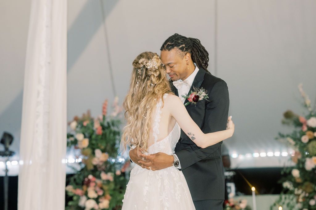 Couple sharing intimate first dance moment at floral-decorated wedding ceremony under tent.