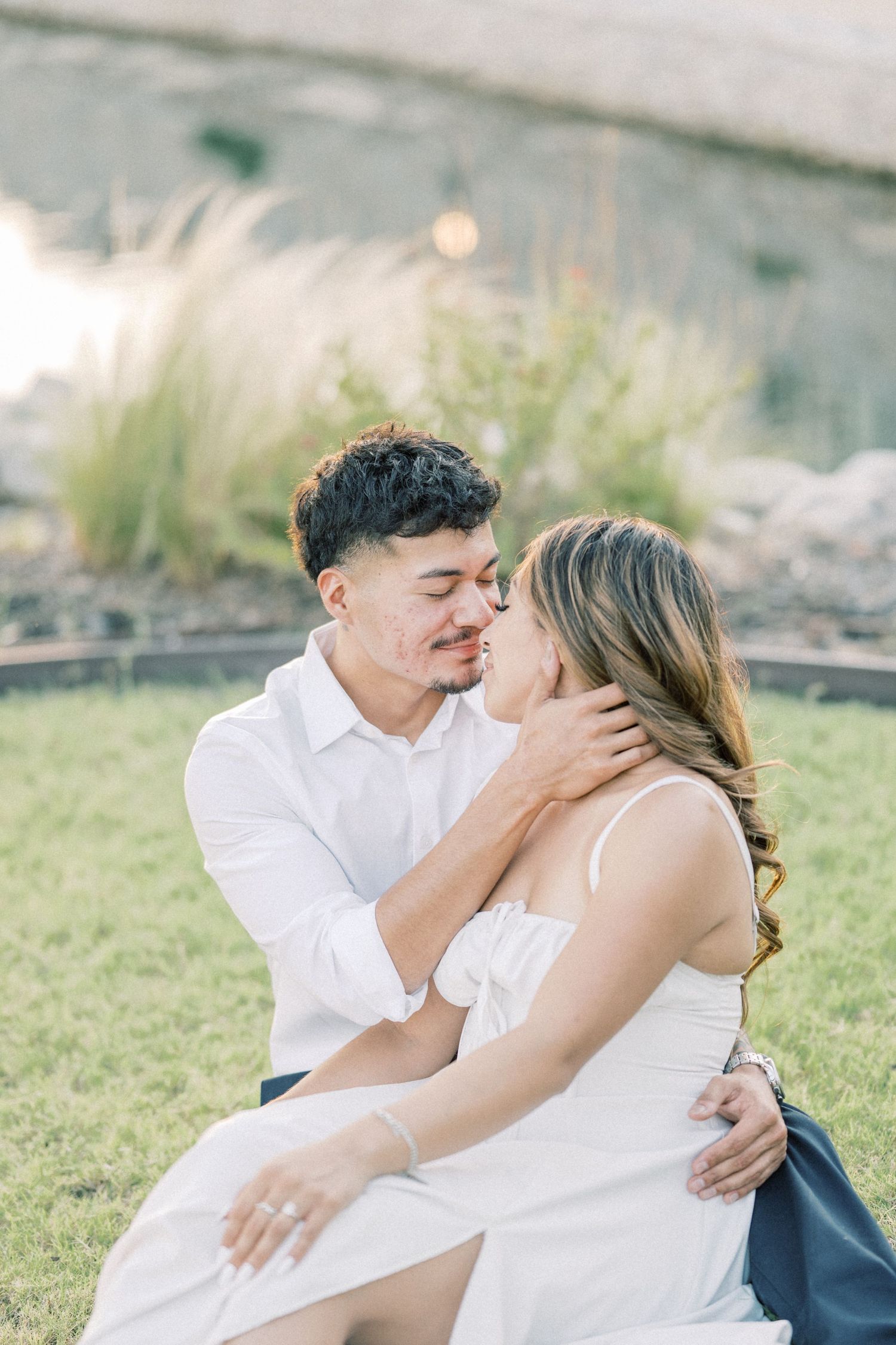 Couple sitting on grass sharing a romantic almost-kiss during golden hour engagement photos.