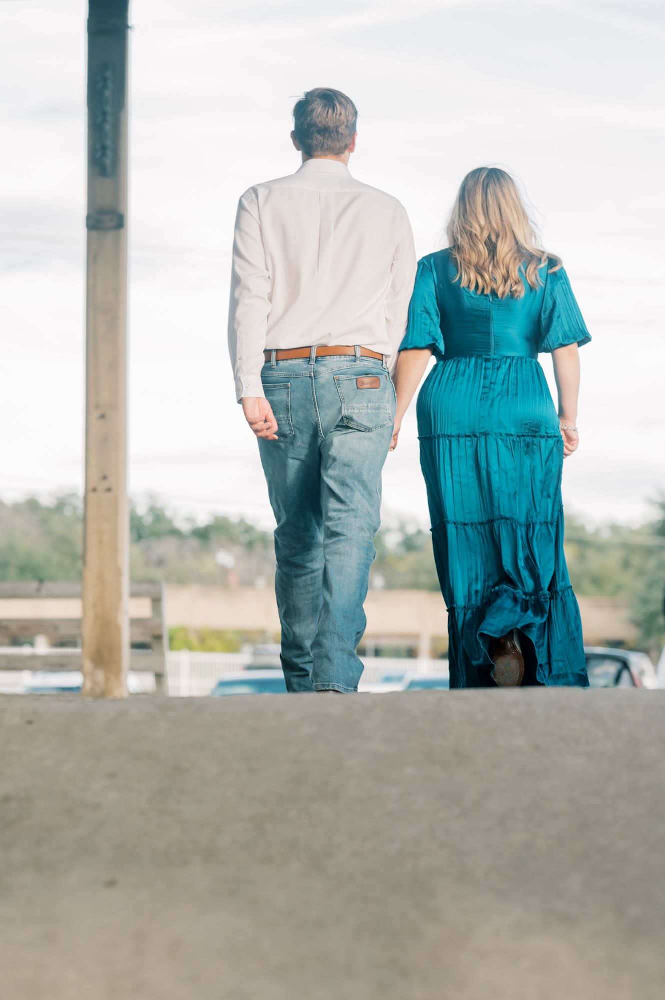 A couple sits together on a bench wearing a blue dress and casual attire while looking out at a scenic view.