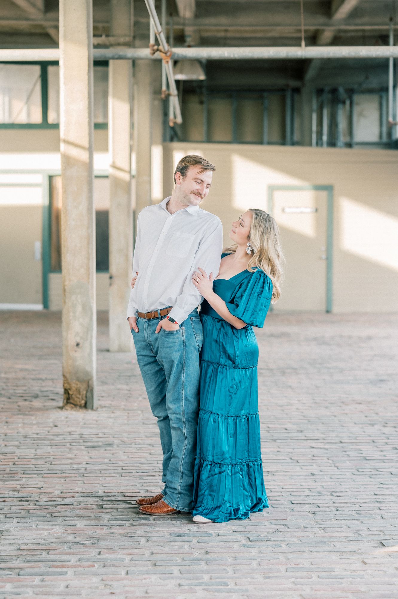 A couple in casual attire dances romantically in an industrial warehouse space with sunlight streaming through windows.