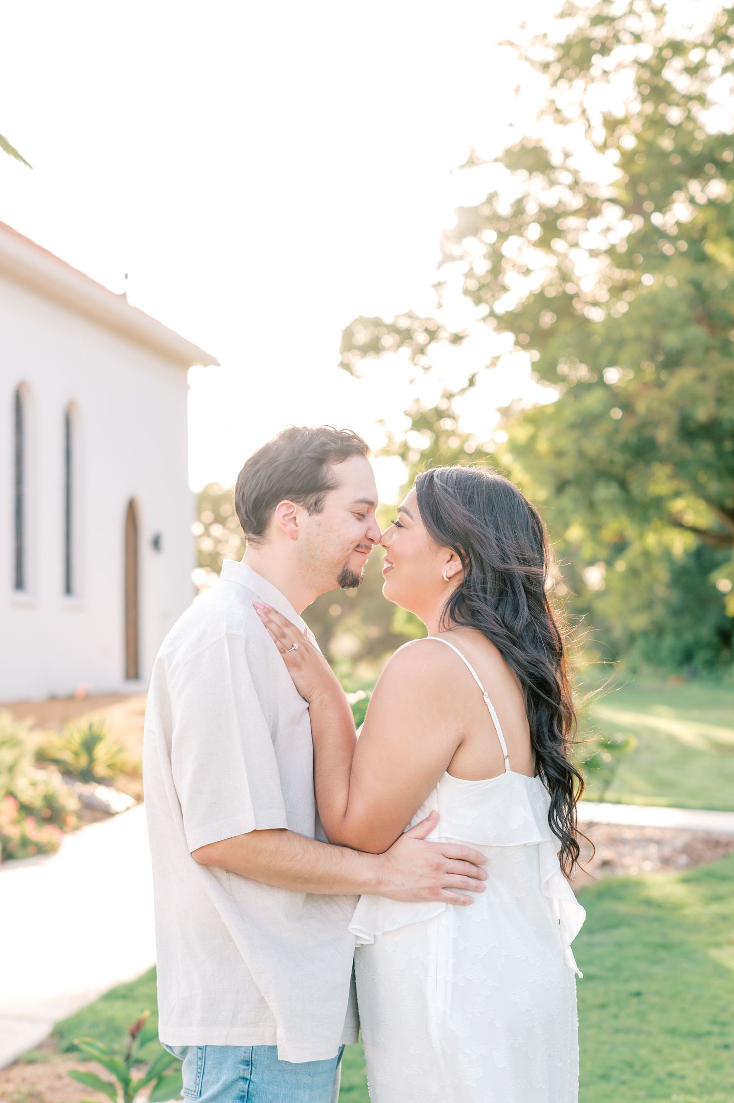 A couple shares tender moments outdoors during a golden hour photoshoot near a white building.