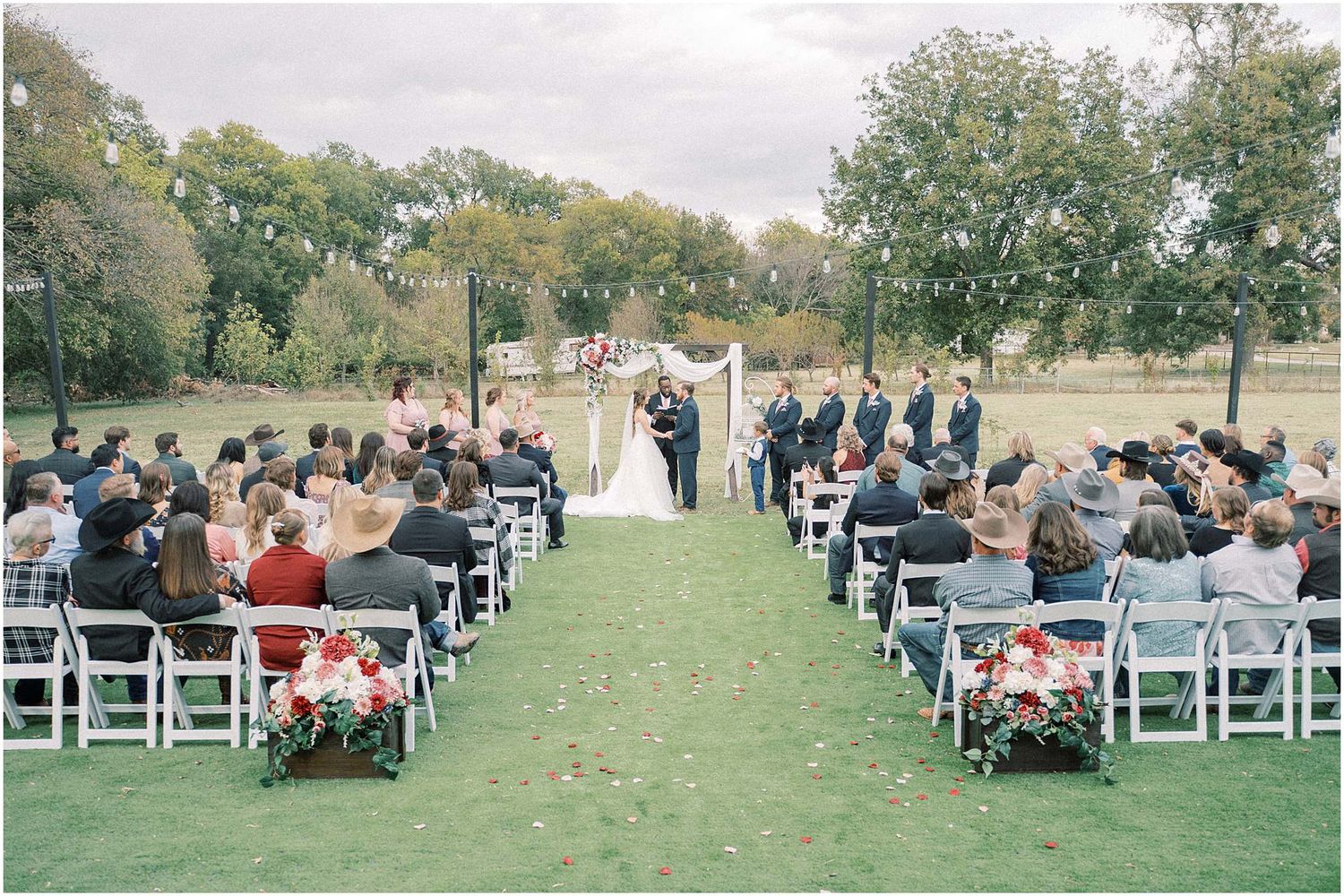 Wide view of outdoor wedding ceremony with white chairs and natural landscape.