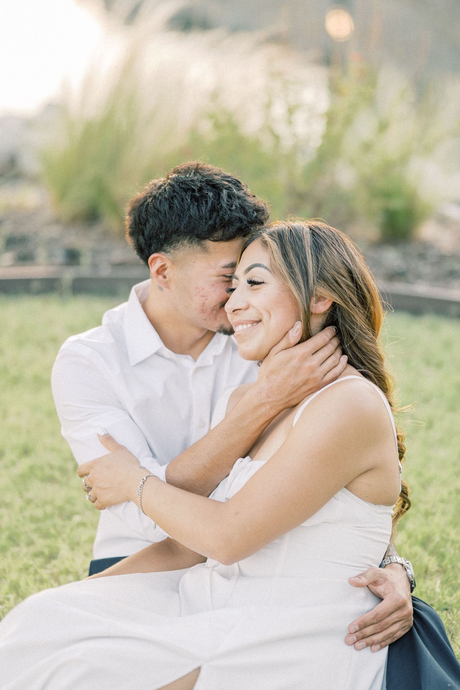 A man tenderly kisses a smiling womans cheek while holding her face during a golden hour session.