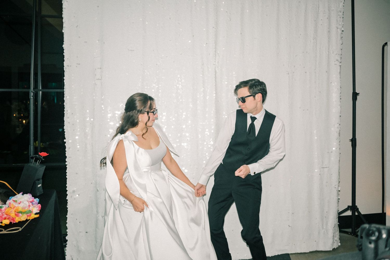 Bride and groom dancing joyfully in front of a sparkling sequin backdrop at their wedding reception.
