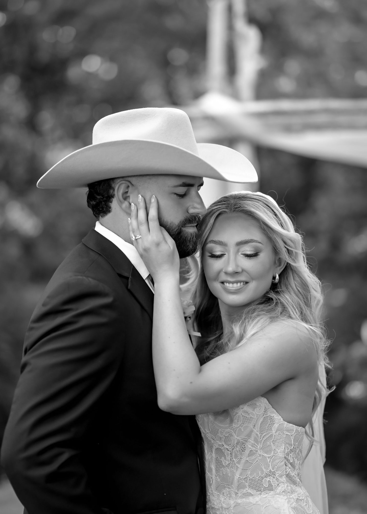 Black and white romantic photo of groom in cowboy hat kissing bride on cheek at wedding.