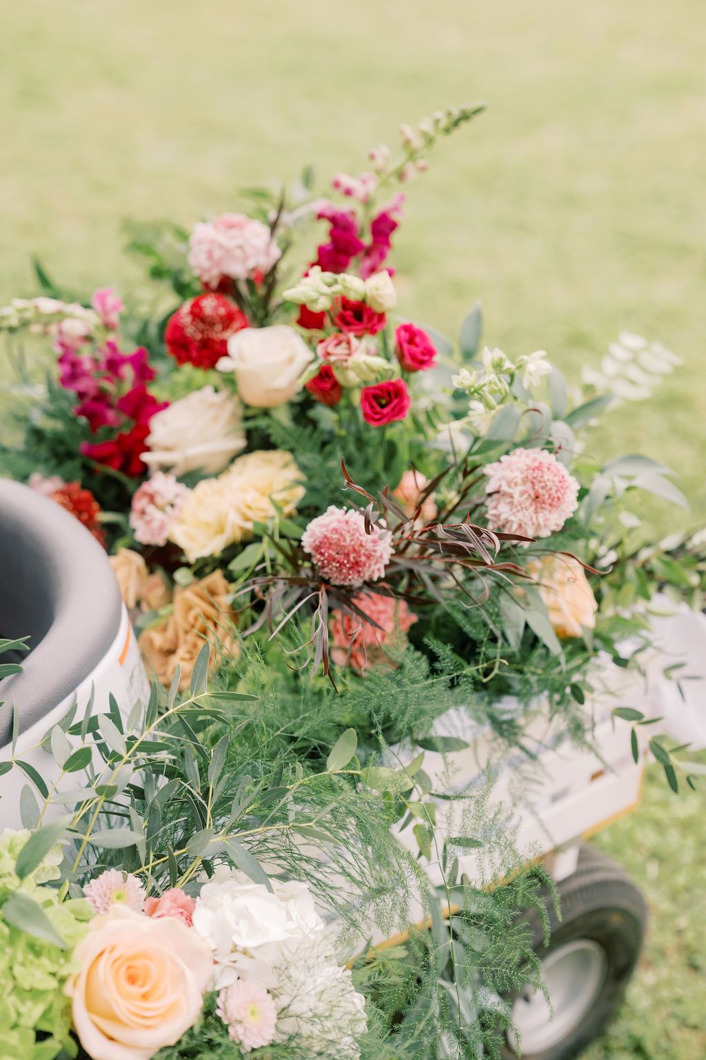 Lush floral arrangement with pink, red, and cream roses and greenery displayed outdoors on a cart.