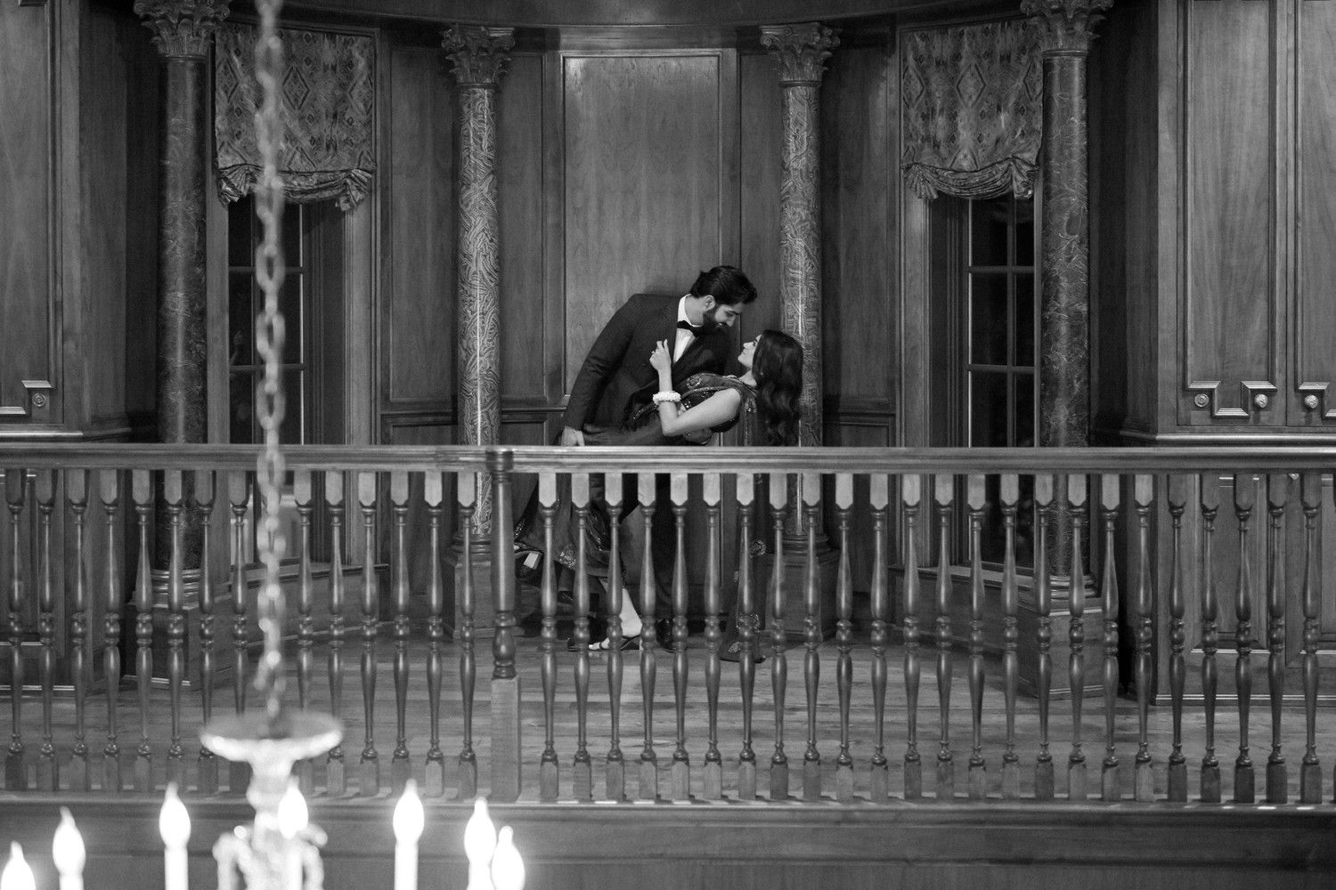 A romantic black and white scene of a couple embracing on an ornate balcony with candles below.