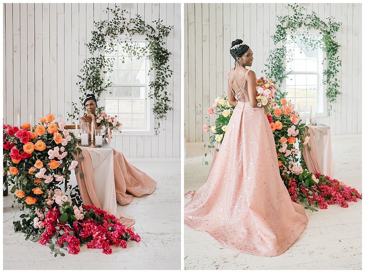 Romantic wedding setup with pink gown and floral arch featuring coral and pink flowers against white paneled wall.