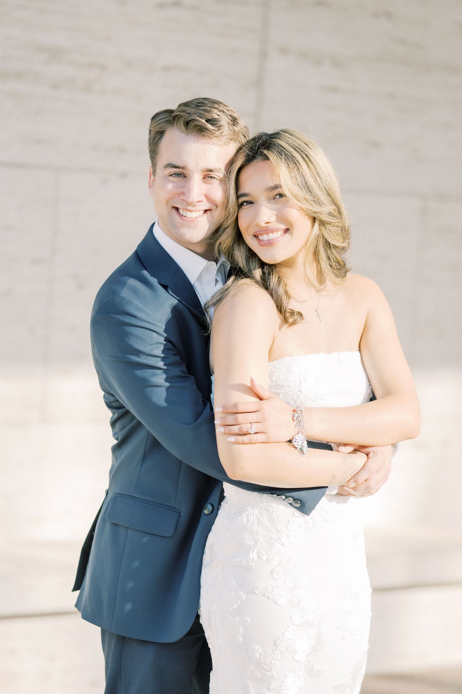A couple in wedding attire share joyful candid moments in a series of three photos against a light wall.