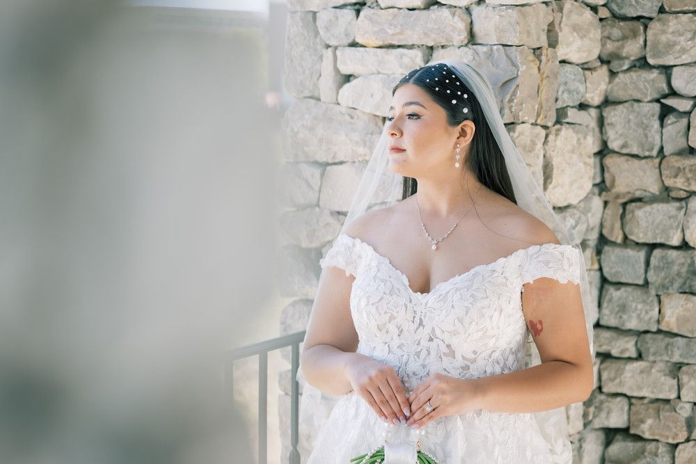 A bride in a flowing white dress stands gracefully beneath stone archways with natural lighting.