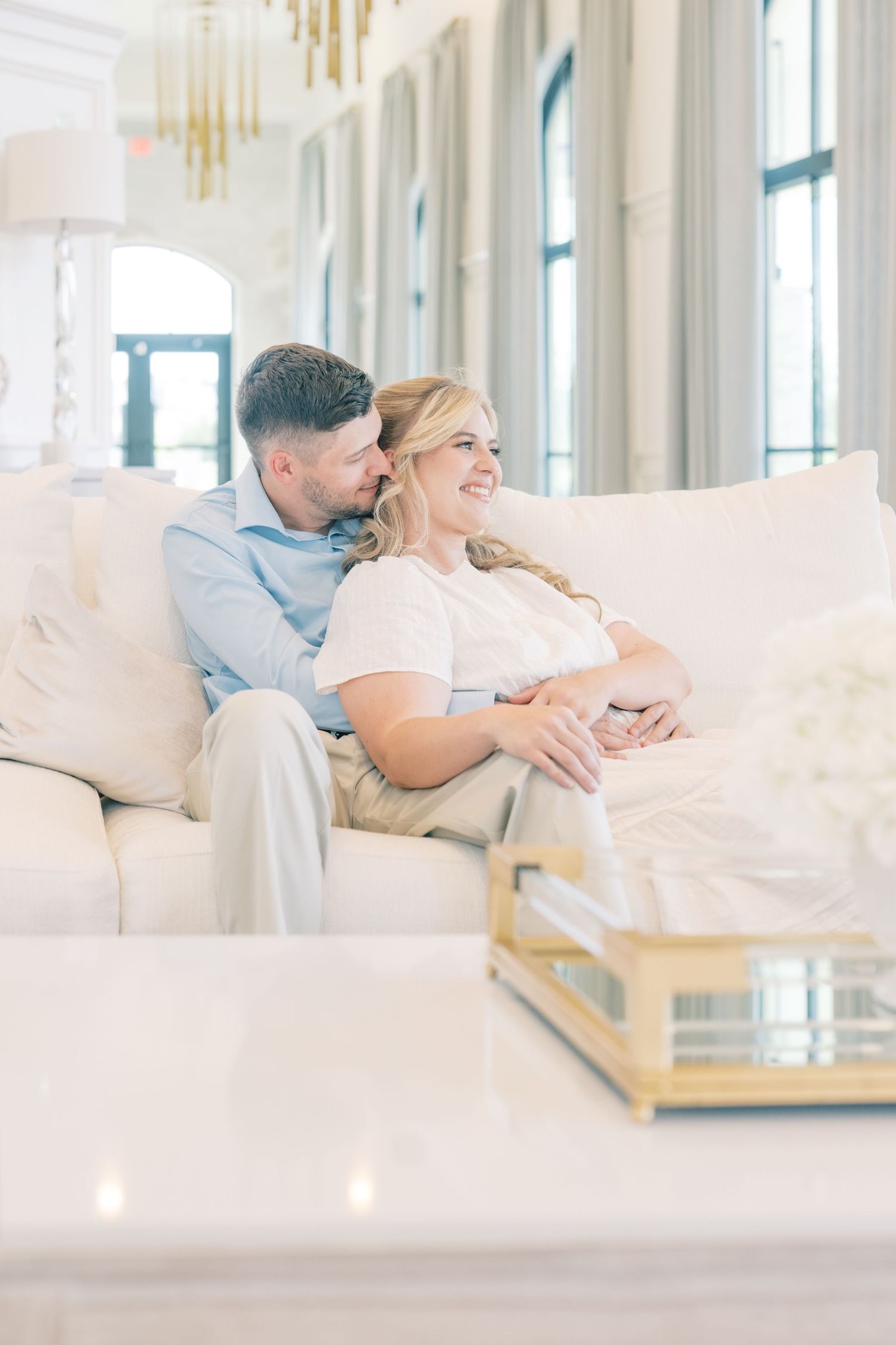 Couple sitting together on a white sofa in an elegant bright interior, smiling and sharing a tender moment.