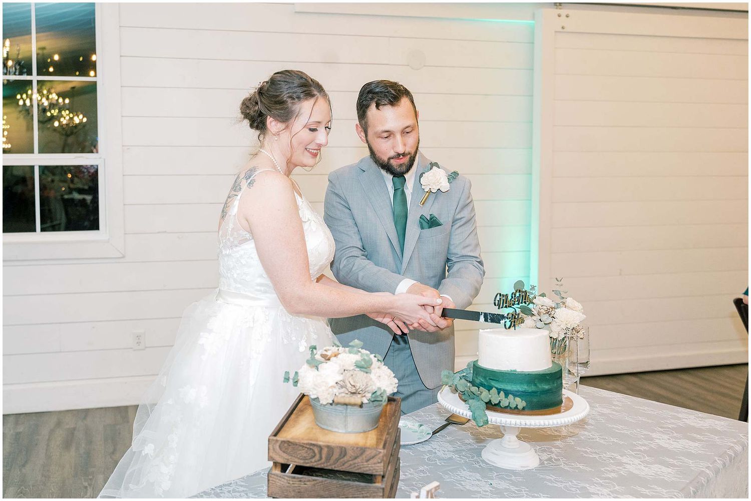 Wedding couple cuts their elegant white and green tiered cake during reception celebration.