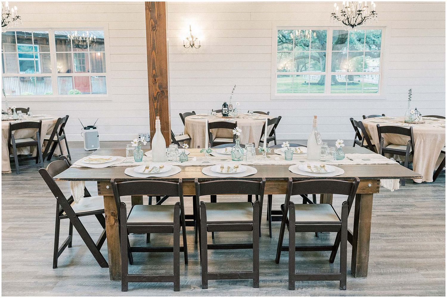 Minimalist wedding reception setup with long wooden tables and black chairs in a bright white-walled venue.