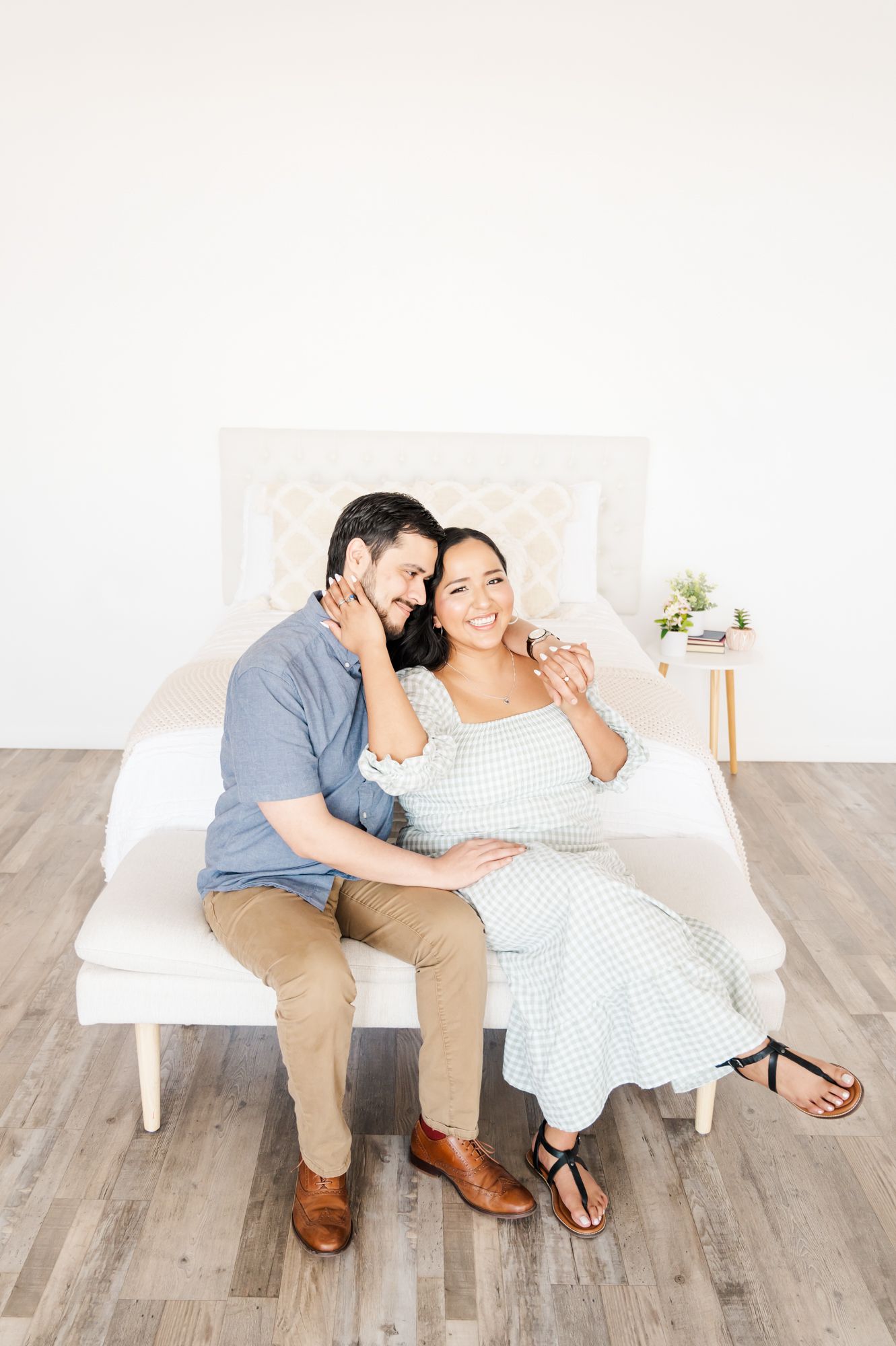 Two people embrace while seated on a white chair against a minimalist backdrop.