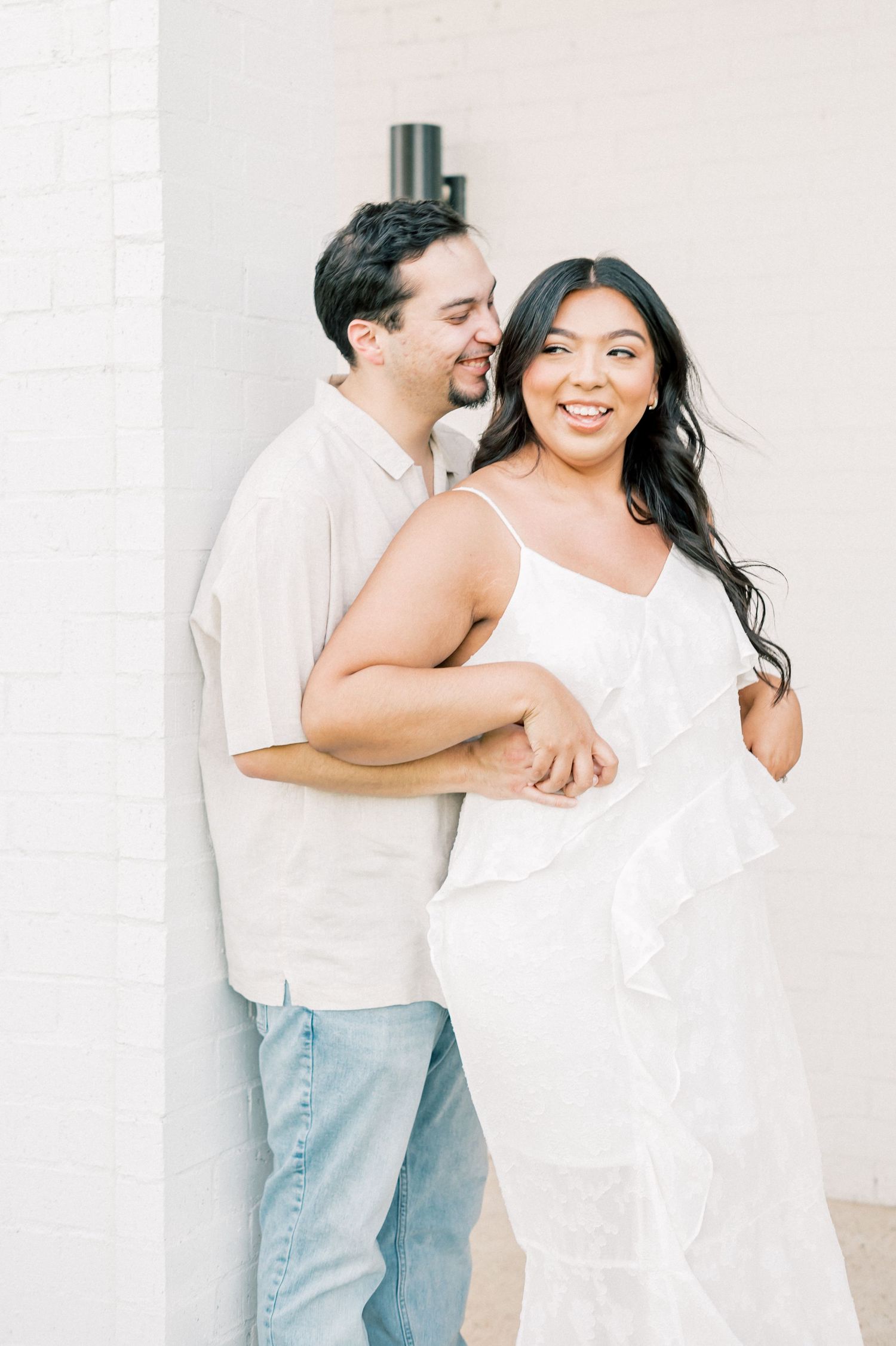 A couple wearing white and light denim share playful moments in a bright minimalist setting.