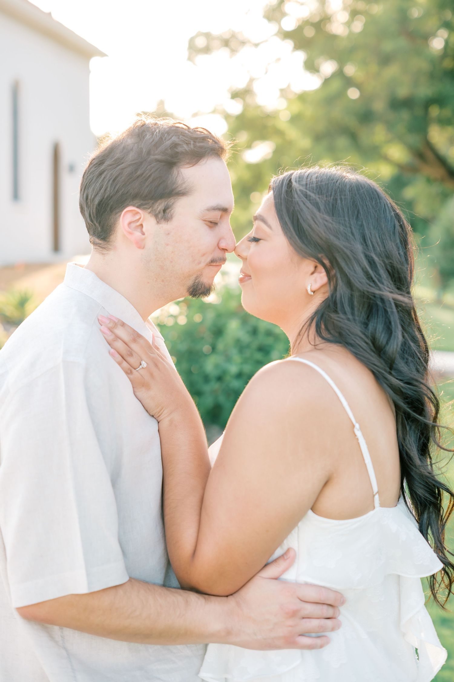 An intimate couple shares a tender moment in white clothing during a golden hour outdoor photoshoot.