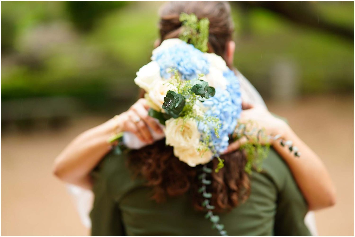 Bride holding a stunning bouquet of blue hydrangeas and white roses while embracing her partner outdoors.