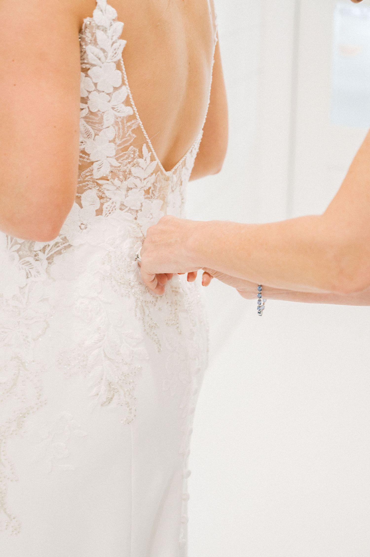 Close-up details of delicate white lace and buttons on the back of a wedding dress.