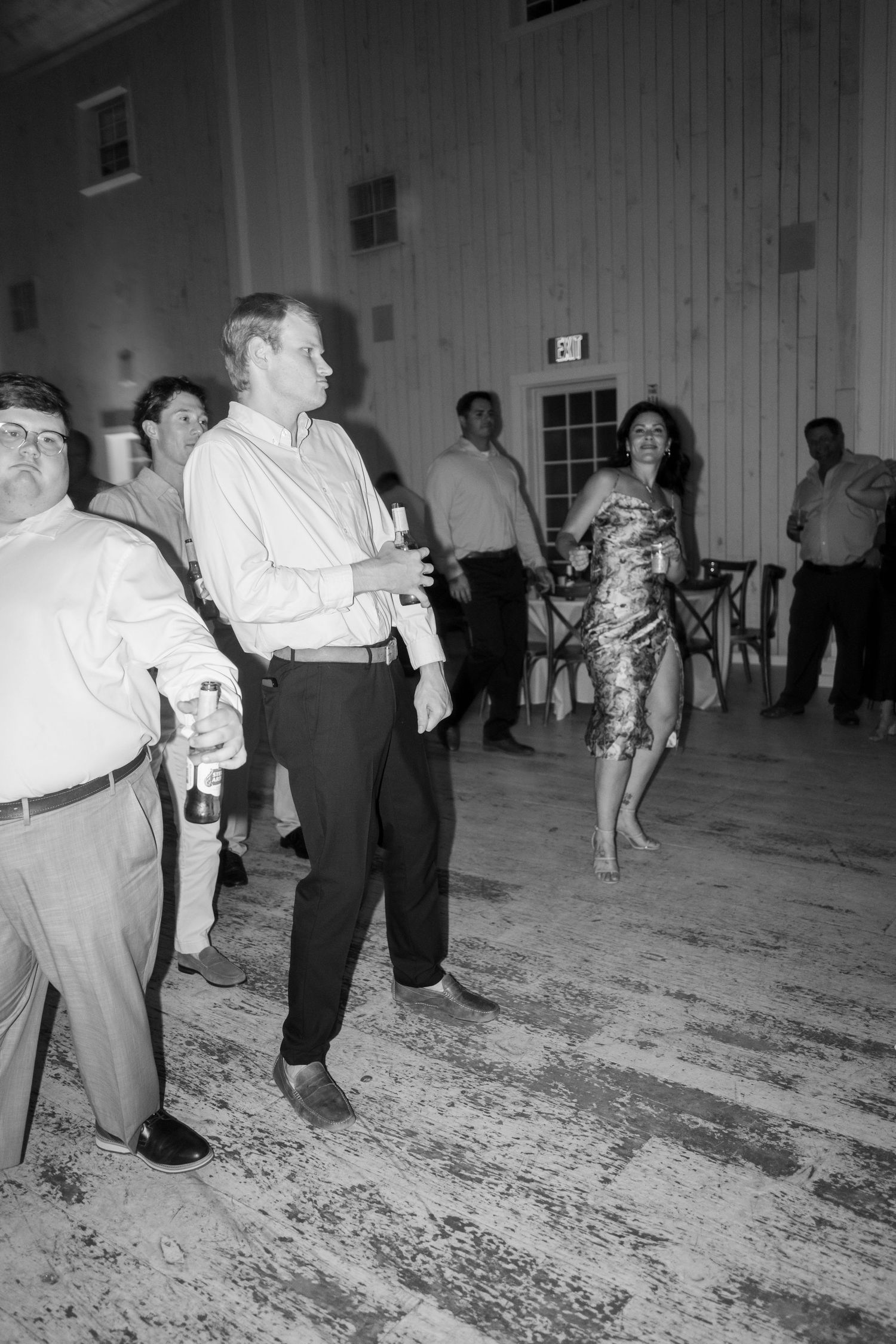 Black and white photo of wedding guests dancing and socializing on a dance floor at a reception.