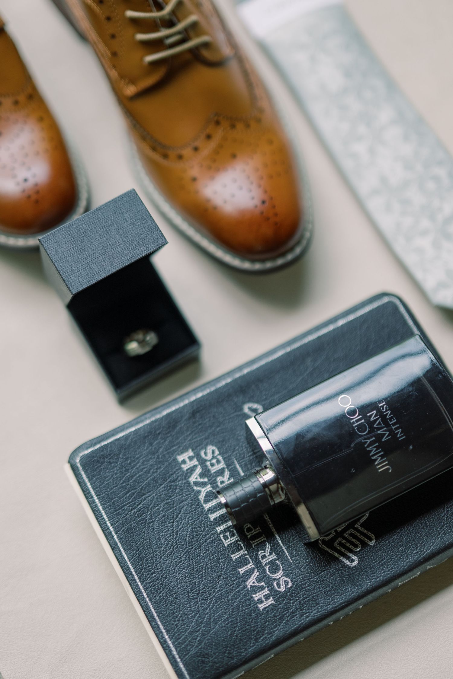 Groom's wedding day details including tan leather brogue shoes, cologne, cufflinks, and a pocket square on a neutral surface.