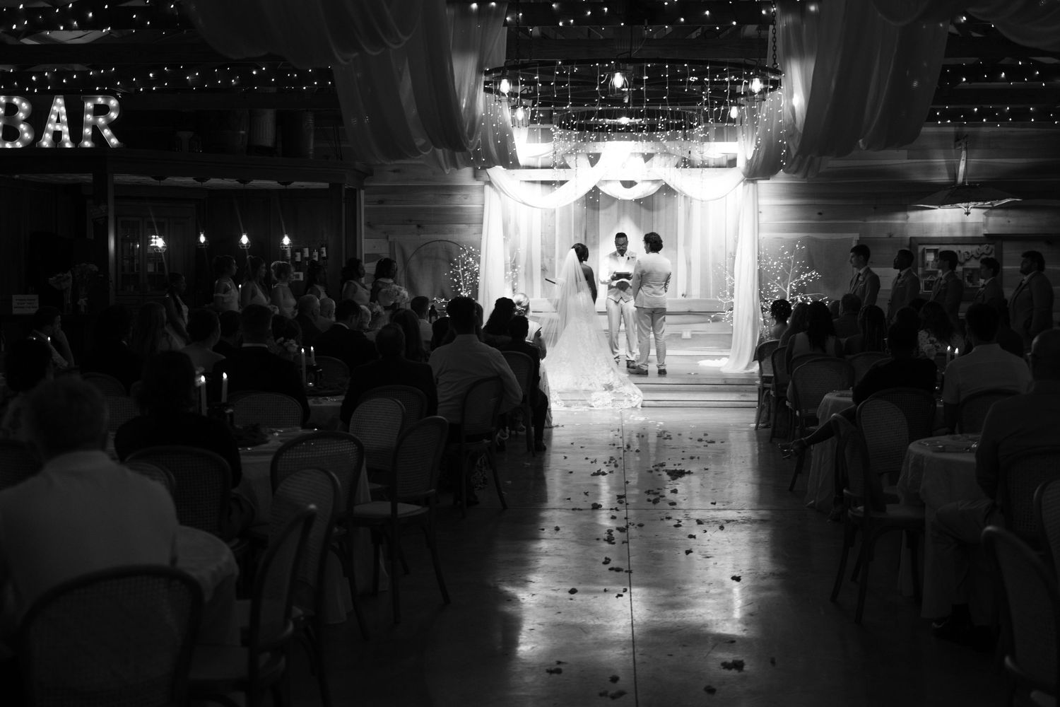 Black and white photo of a wedding couple walking down the aisle in an elegant decorated barn venue.