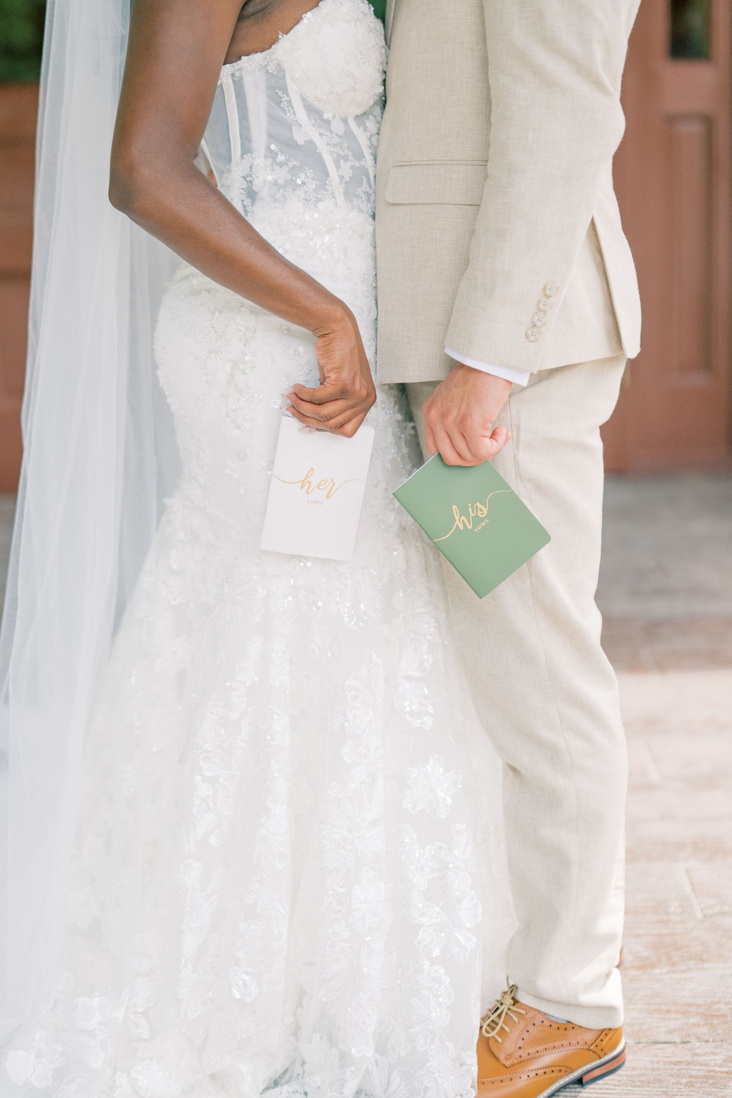 Interracial wedding couple holding his and hers vow books in white and sage green during outdoor ceremony.