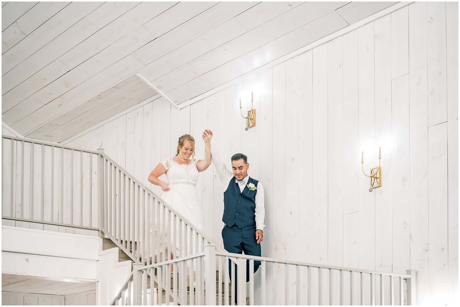 Elegant couple descends white staircase at wedding venue in romantic candlelit atmosphere.