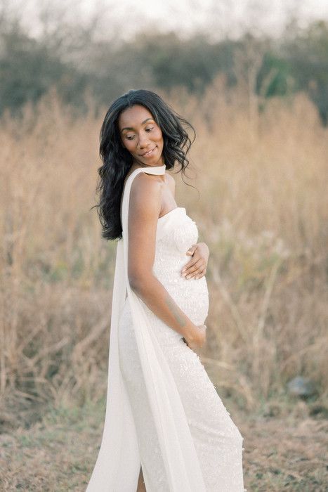 Ethereal maternity photoshoot in a golden field with flowing white dress and veil creating a dreamy atmosphere.