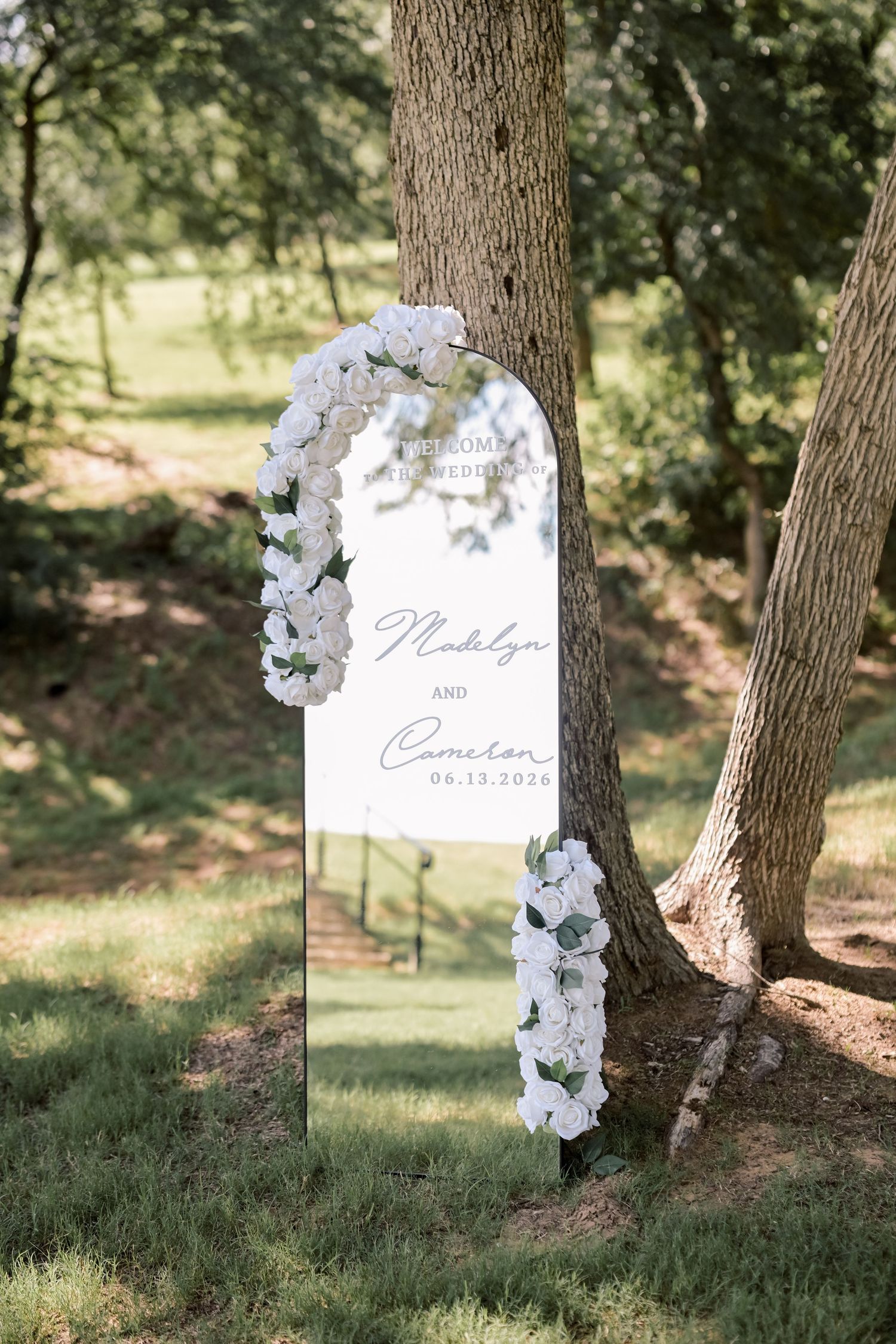 Mirrored wedding welcome sign with white floral arch for Madilyn and Cameron 06.13.2024.