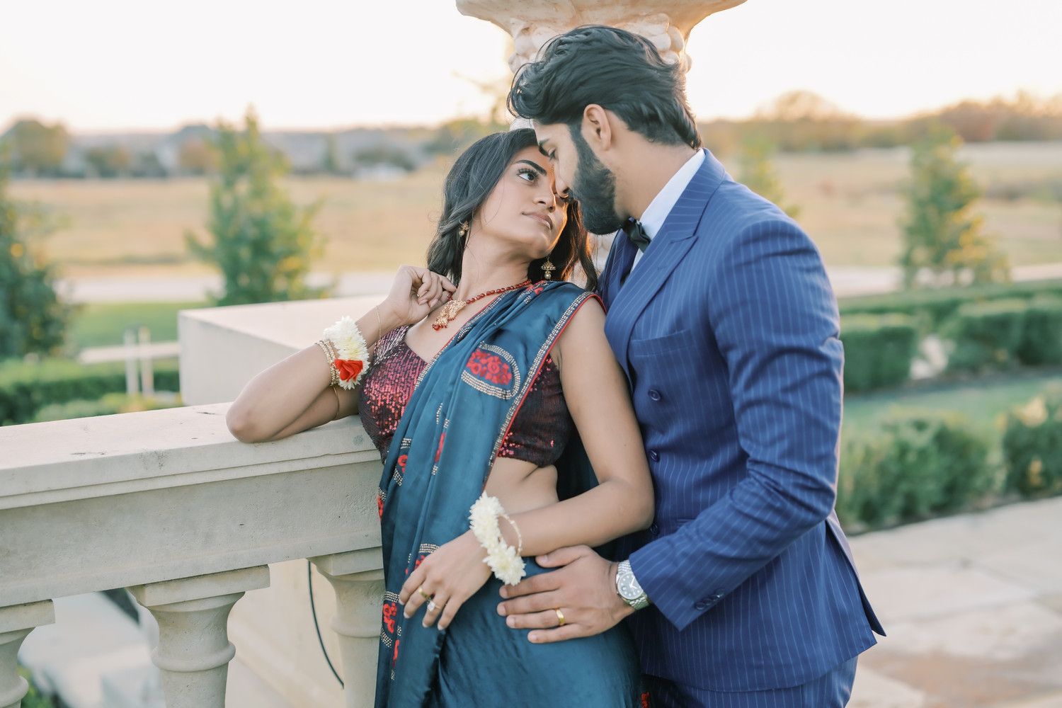 Couple in formal attire embraces on outdoor terrace during sunset.