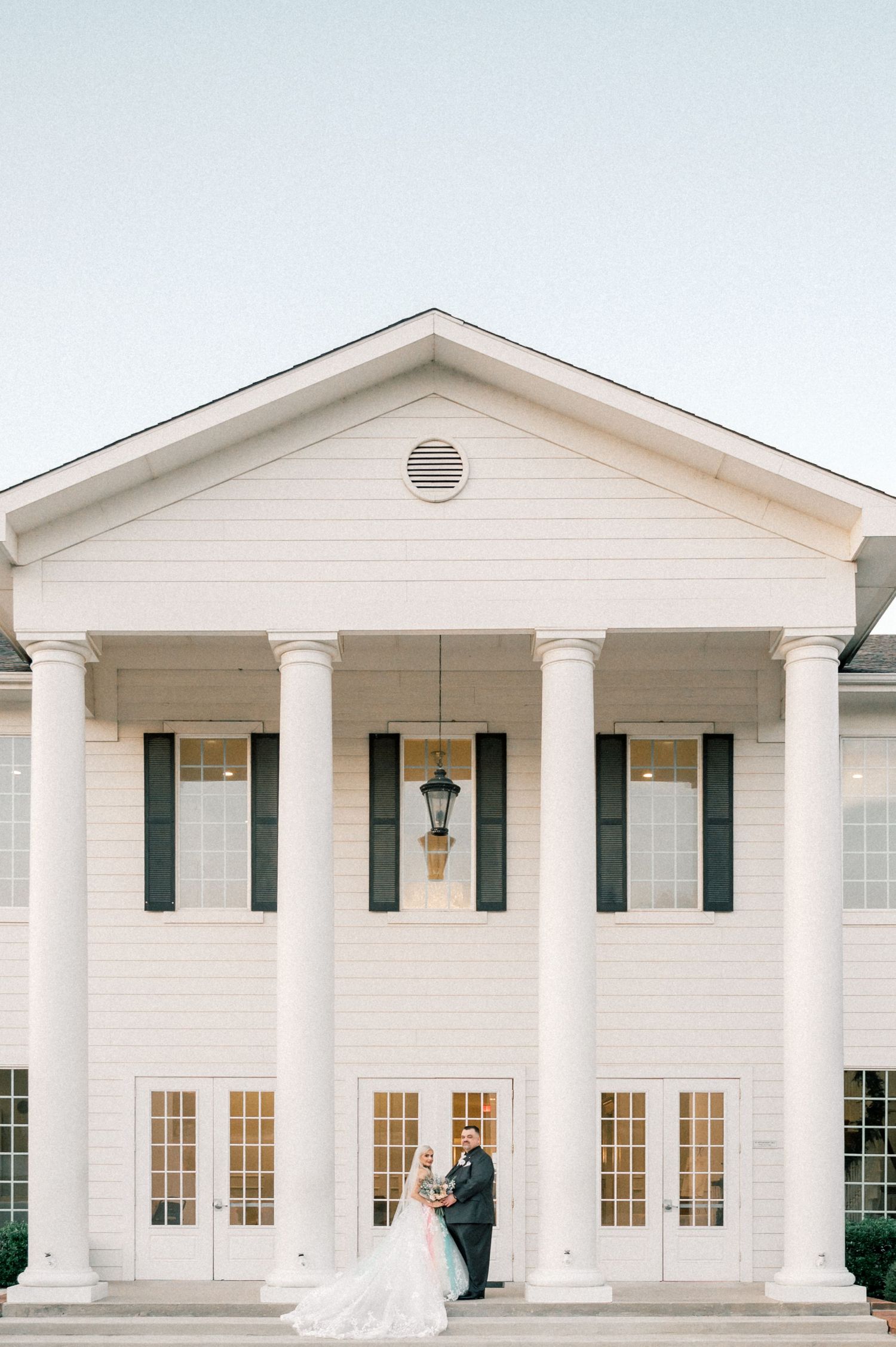 Elegant white colonial style wedding venue with pillars and symmetrical windows.