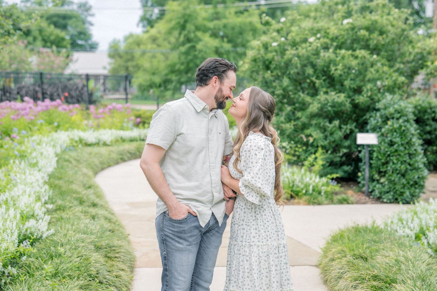 Couple sharing a romantic moment on a garden path surrounded by lush greenery and colorful flowers.