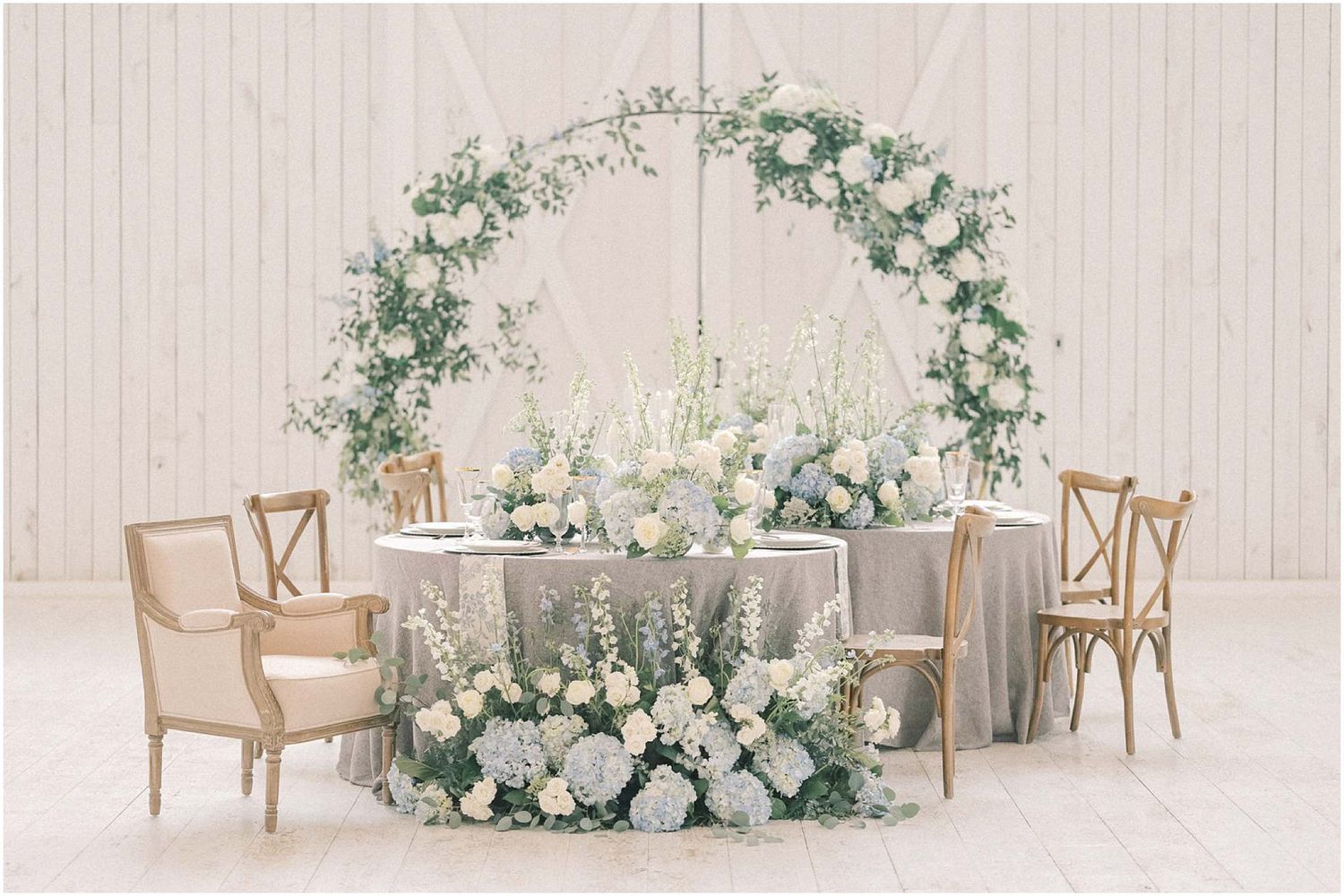 Light and airy wedding reception venue with wooden crossback chairs and white floral centerpieces.