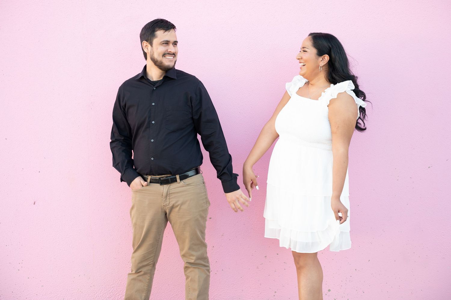 A couple shares a joyful dance moment against a pink background.