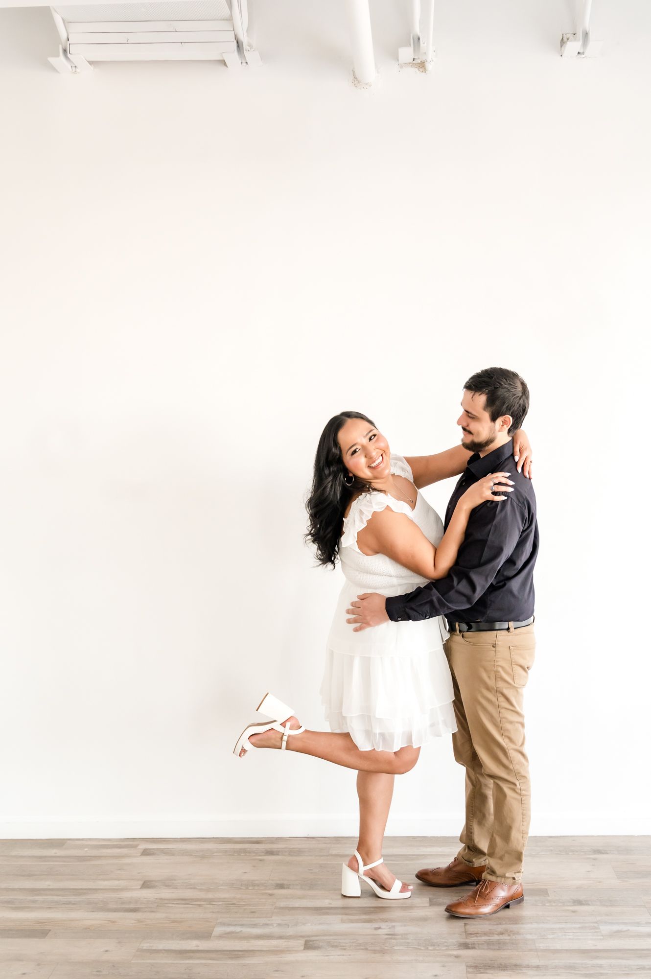 A couple performs a romantic dance lift against a bright white studio backdrop.