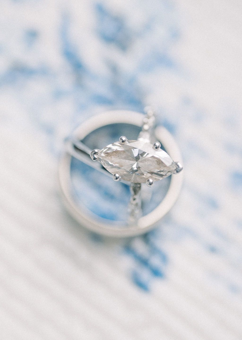 Elegant marquise diamond engagement ring in silver setting displayed on blue and white floral porcelain surface.