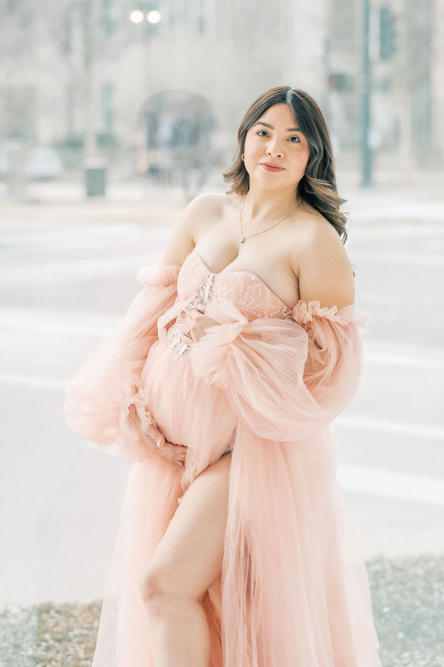 Pregnant woman in elegant blush pink tulle maternity gown posing outdoors for a maternity photo session.