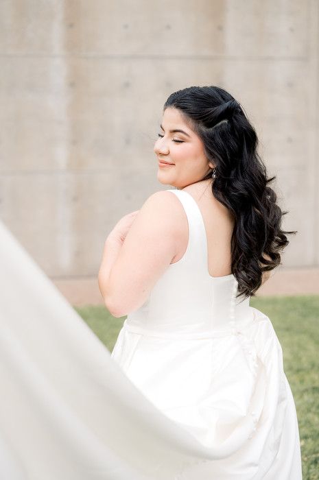 Bride with dark wavy hair in sleeveless white gown posing gracefully with eyes closed.
