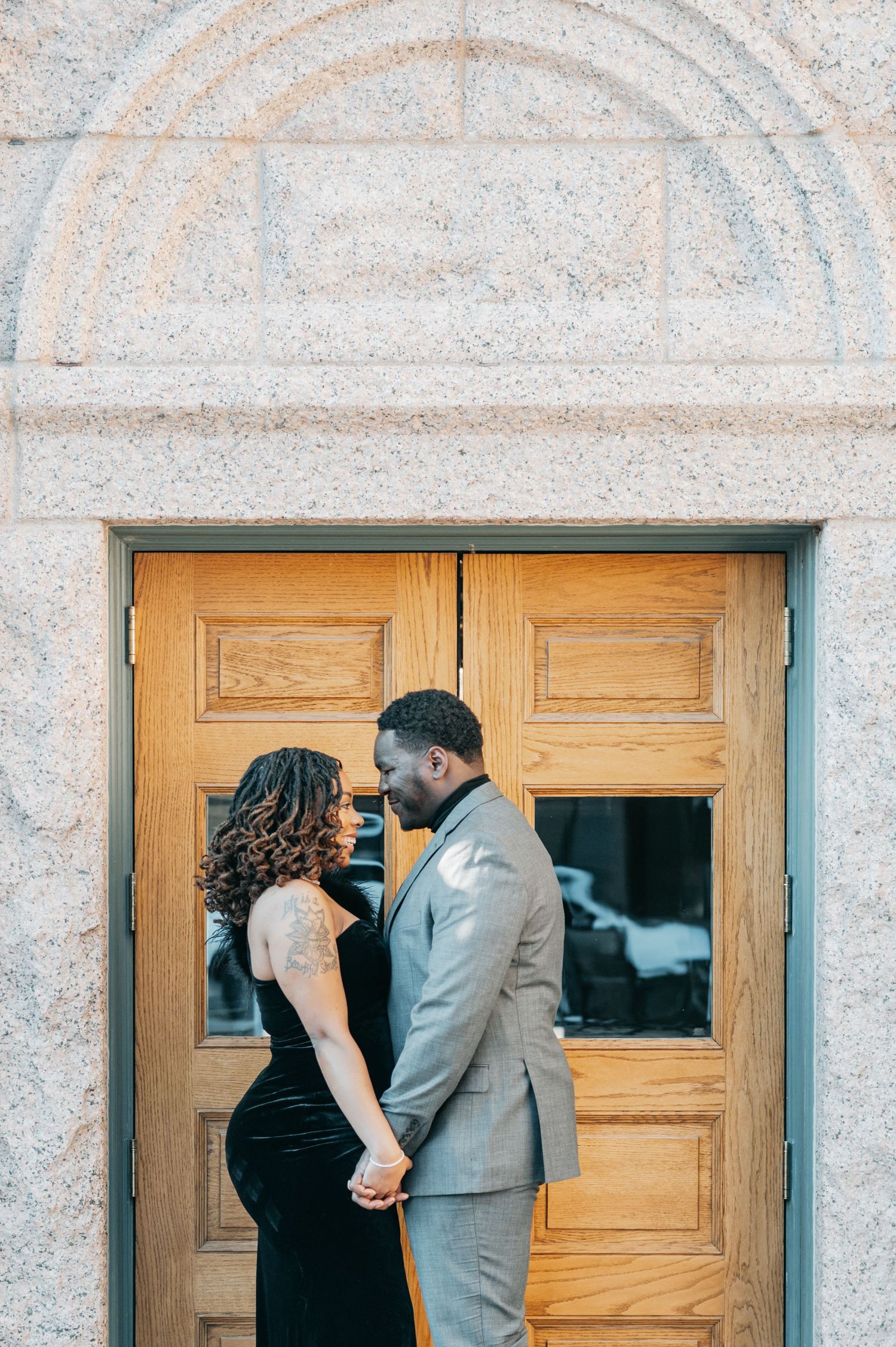Couple holding hands and facing each other in front of elegant wooden doors during an engagement photo session.