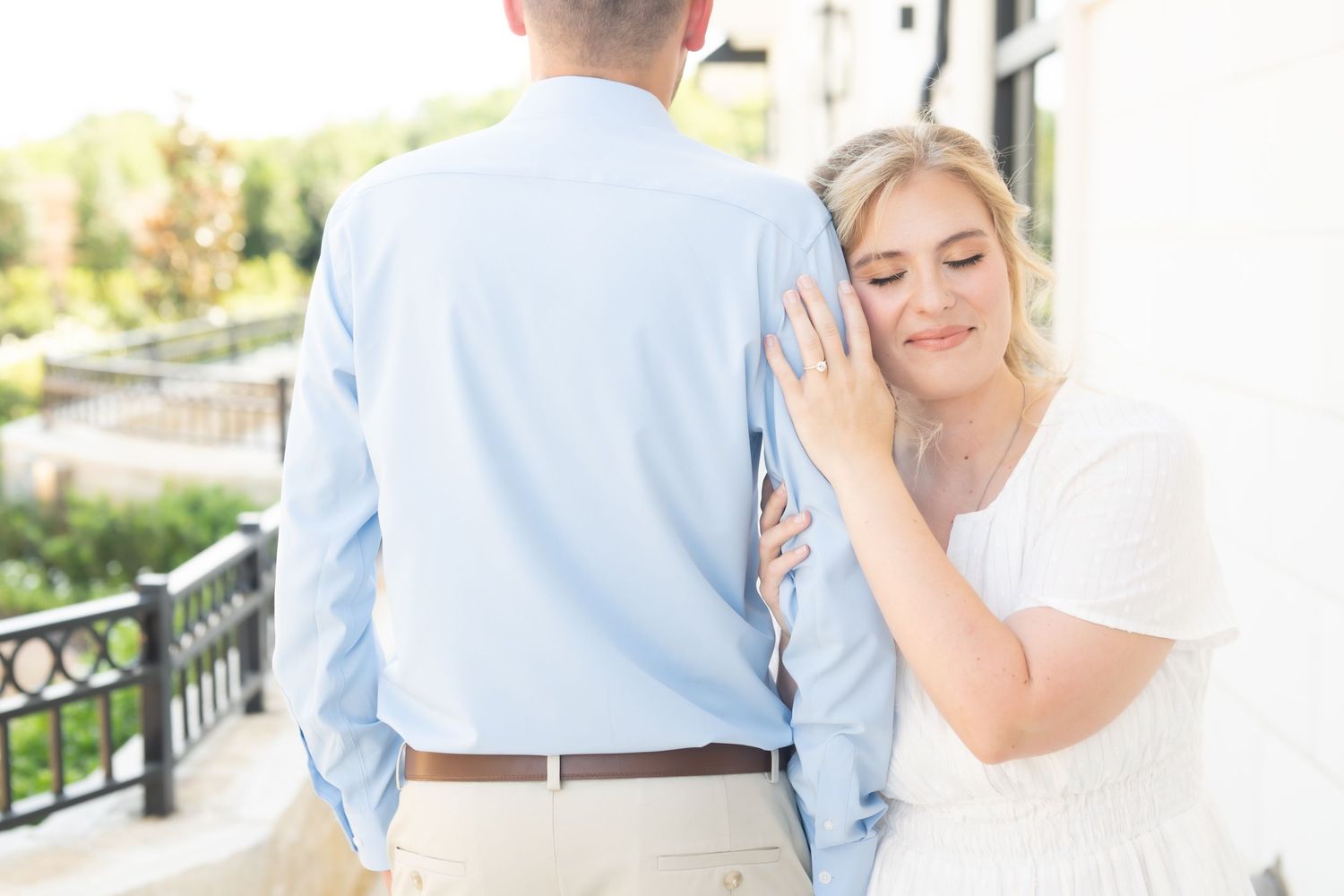 A bride leans her head on a groom's back during an outdoor engagement photo session.