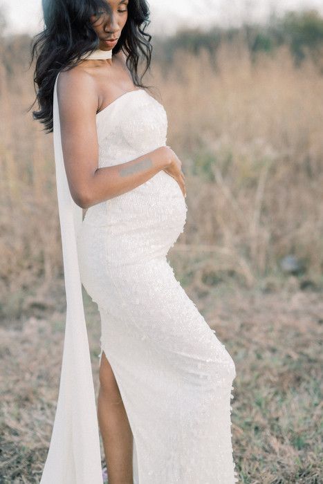 An elegant maternity portrait shows a white strapless gown against a natural outdoor backdrop.