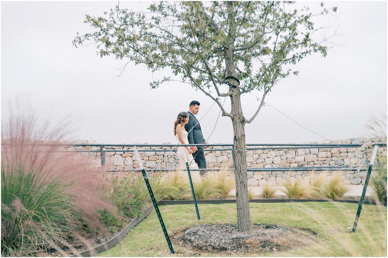 Wedding portraits captured in a garden setting with ornamental grasses and stone wall details.