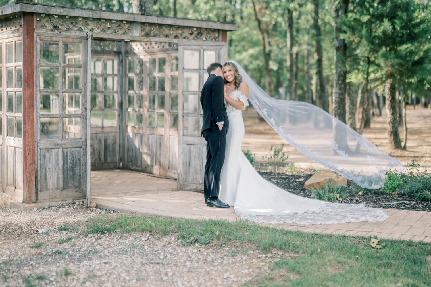 Bride and groom share romantic kiss near rustic wooden gazebo with flowing veil in outdoor forest wedding setting.