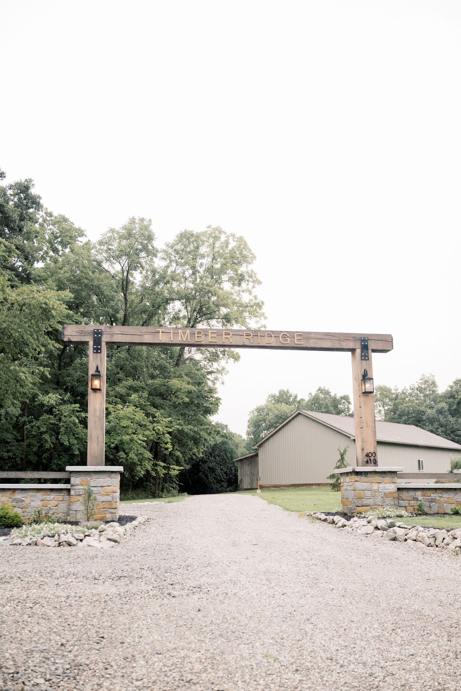 Wooden entrance arch with lanterns marks the gravel driveway entry to Timber Ridge wedding venue.