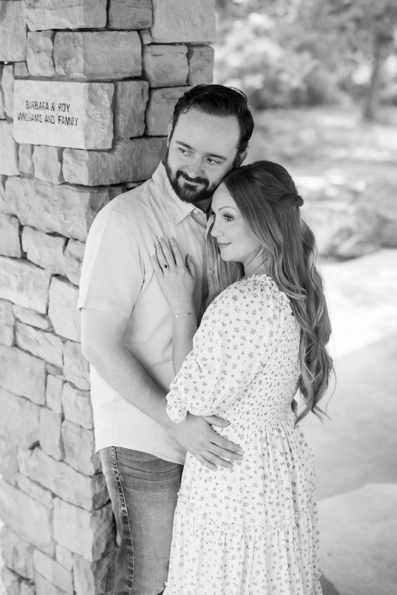 Black and white photo of couple leaning against a stone pillar in a garden.
