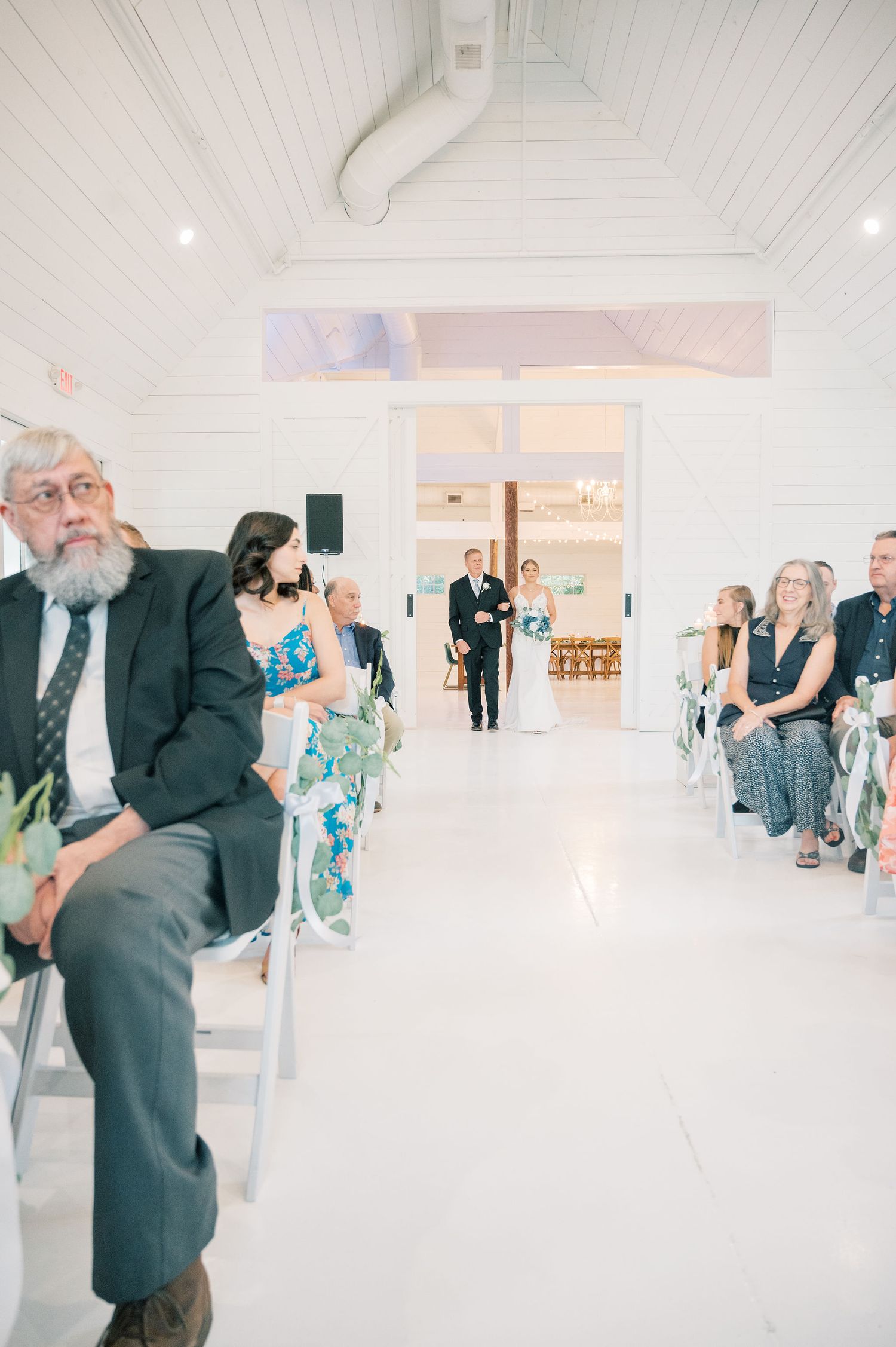 Wedding guests mingle in a modern white church venue with vaulted ceilings and natural lighting.