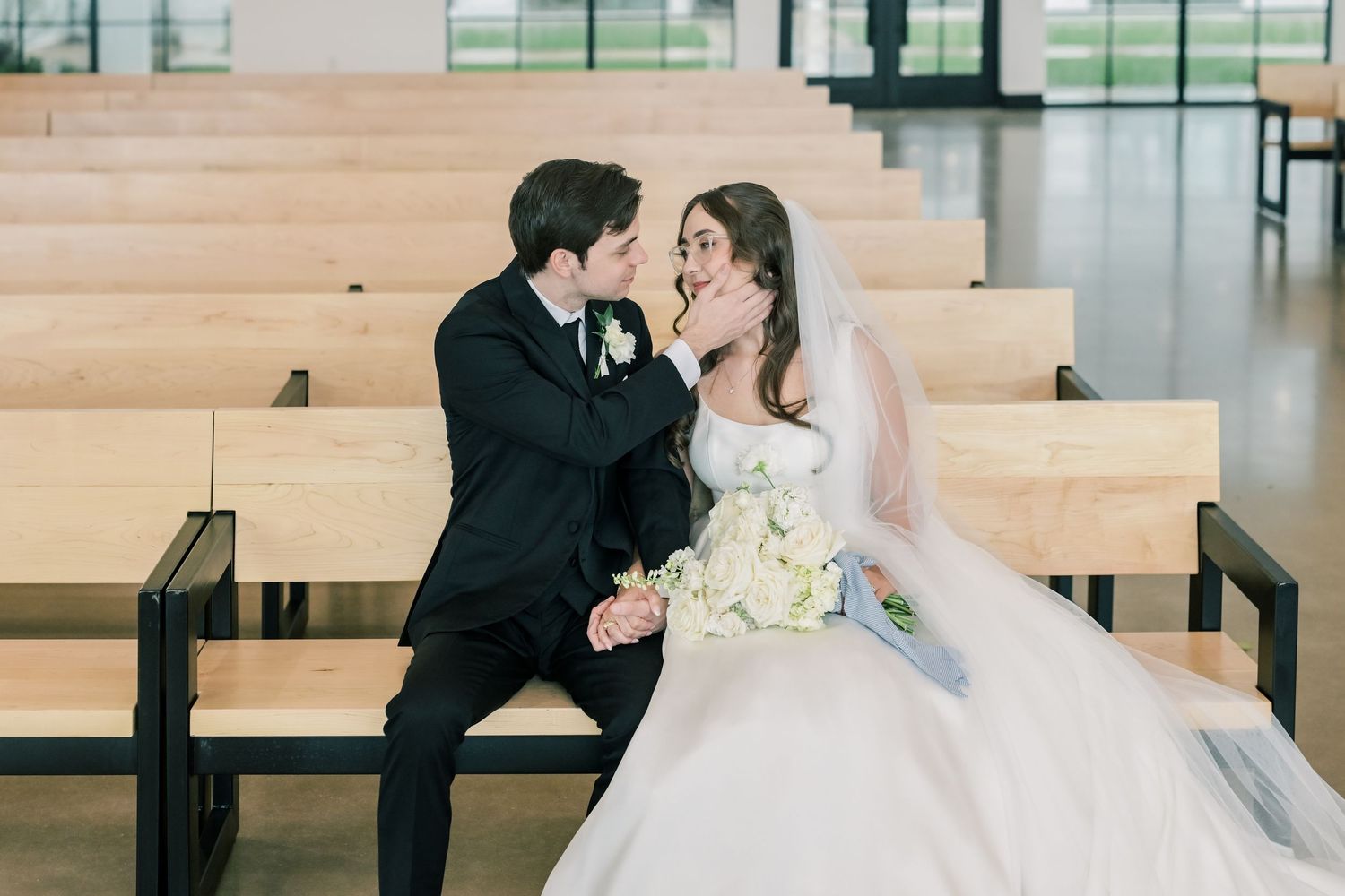 Bride and groom sharing romantic moment on wooden bench in modern chapel.