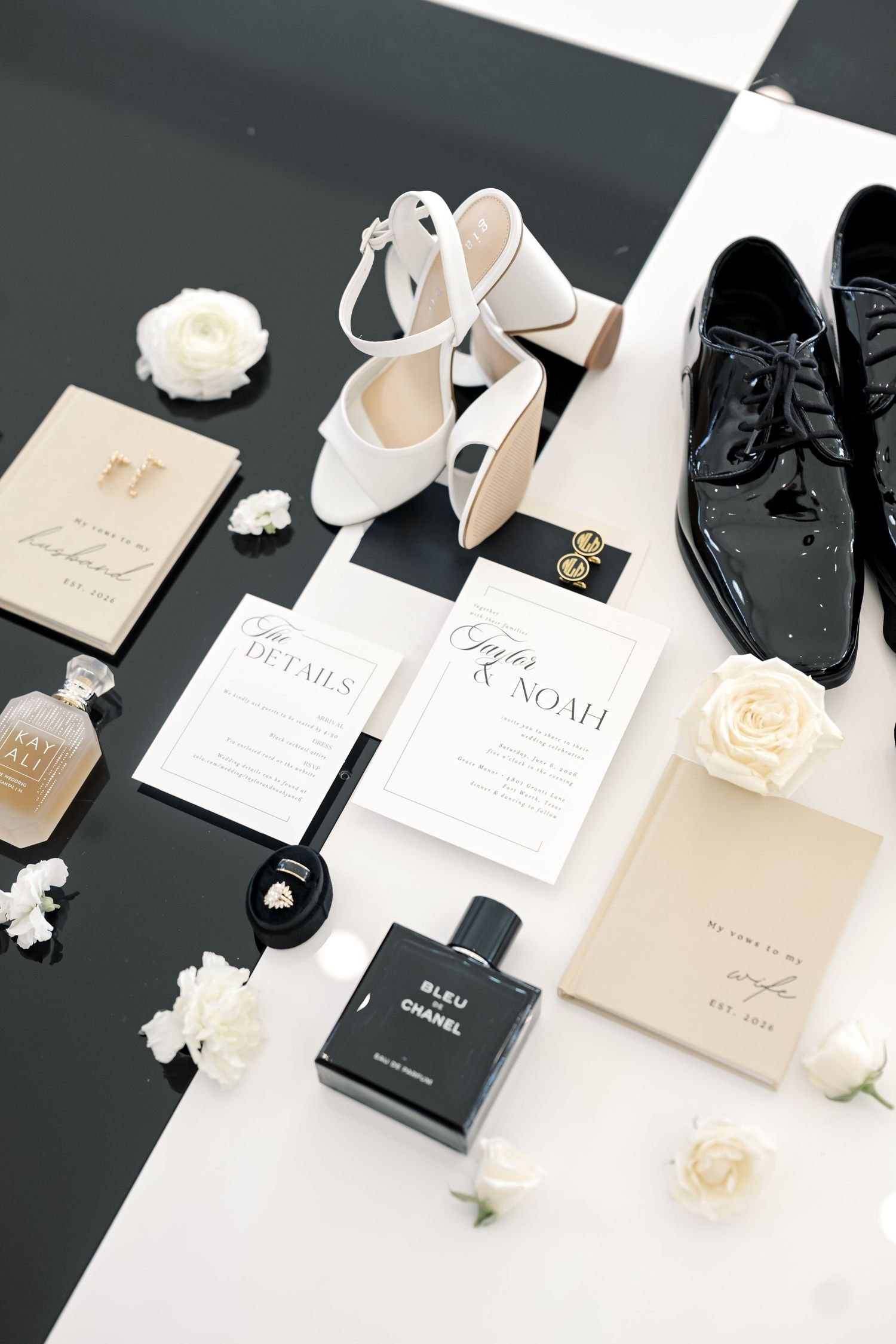Elegant wedding flat lay with Chanel perfume, white heels, patent shoes, floral invitations, and white roses on black and white background.